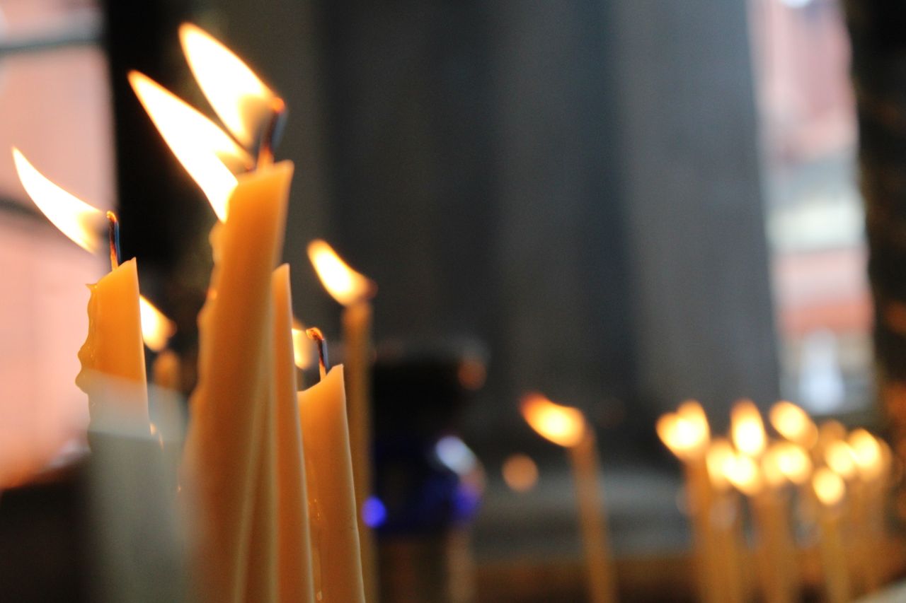 Rows of glowing candles in a dim indoor setting, evoking a serene and spiritual mood.