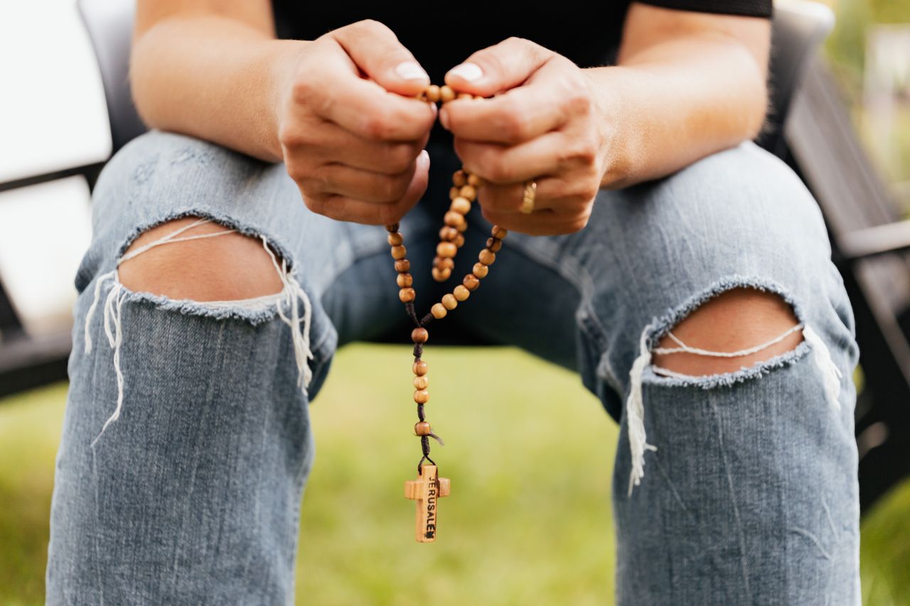 Close-up of a person holding rosary beads in a moment of prayer outdoors, expressing faith.