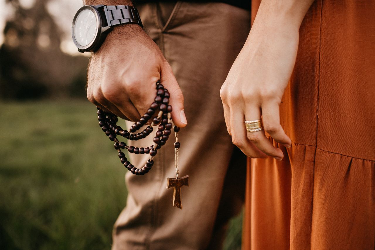 Side view of crop anonymous male with cross on beads and wristwatch standing close to female partner on meadow