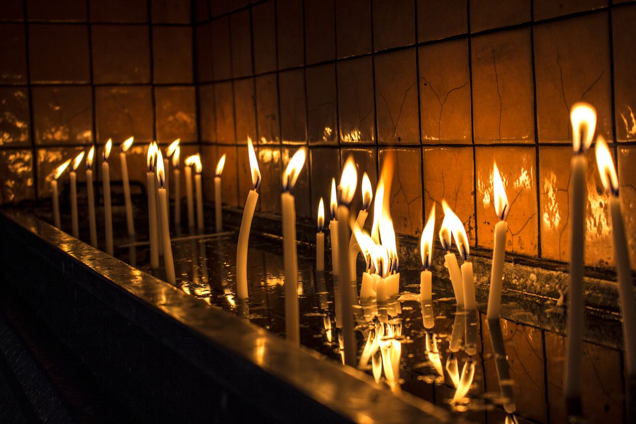 Lit candles reflecting on a dark surface in a tranquil setting, evoking warmth and serenity.